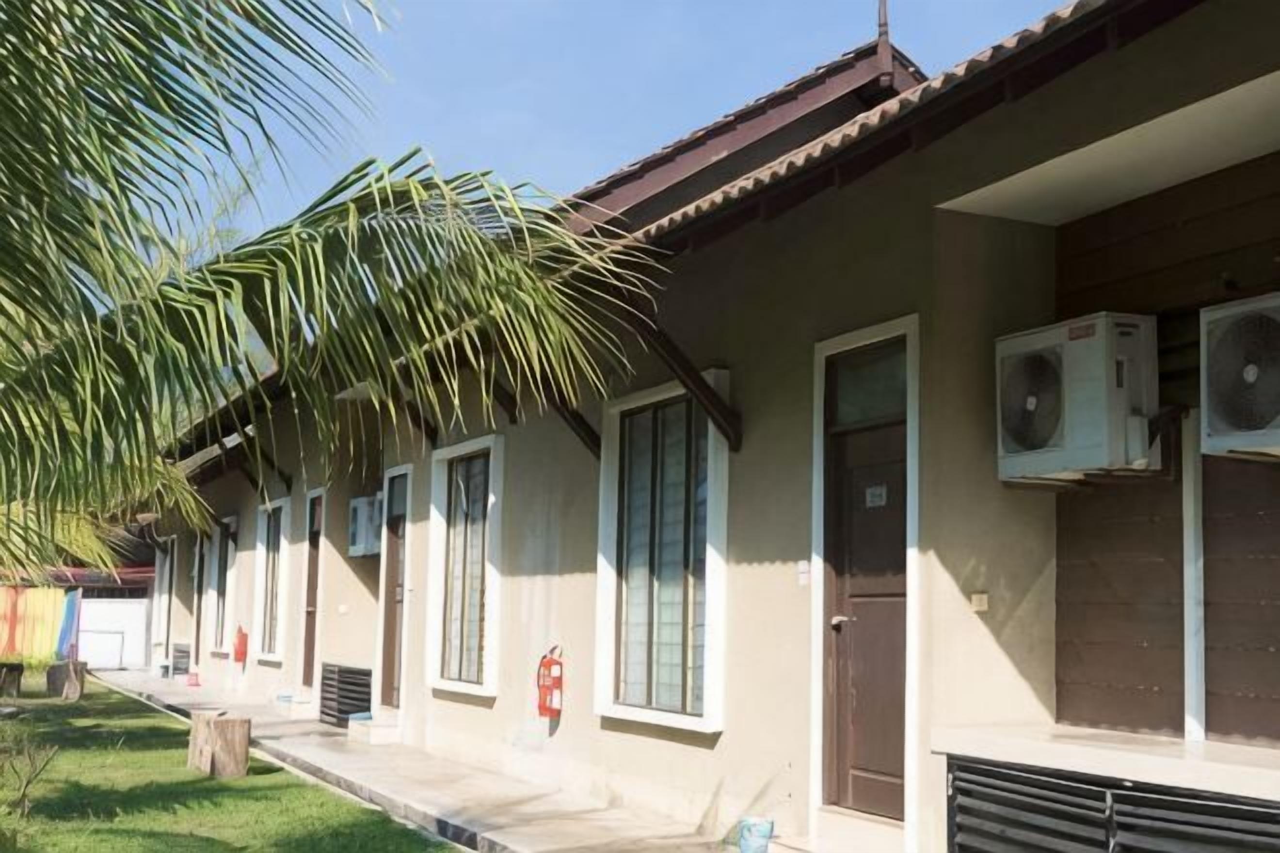 Uma fileira de edifícios térreos com grandes janelas, aparelhos de ar condicionado e uma palmeira em primeiro plano.