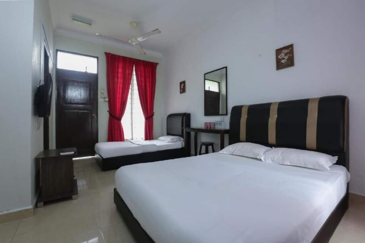 A hotel room with a large bed, a smaller bed, a desk, a chair, a TV, and a ceiling fan.