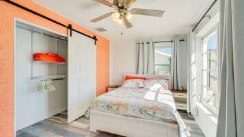Un dormitorio con cama, ventilador de techo, ventana con cortinas y armario con perchero.