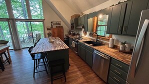 A modern kitchen with dark green cabinets, a wooden island, and a large window overlooking a deck. - Charming lake front 3-bedroom/loft cabin w/ AC, WiFi in delightful Cub Run, KY. (Cub Run)