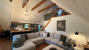A spacious living area with a large L-shaped sectional sofa, a wooden dining table, and a kitchen in the background. - Charming lake front 3-bedroom/loft cabin w/ AC, WiFi in delightful Cub Run, KY. (Cub Run)