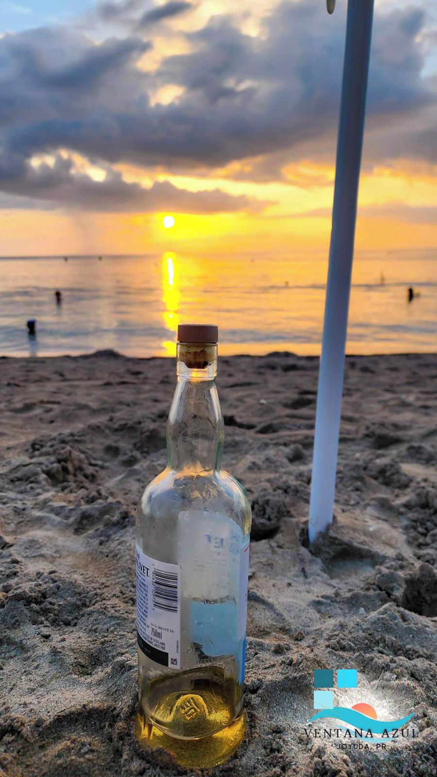 En flaske på en sandstrand med solnedgang i baggrunden.
