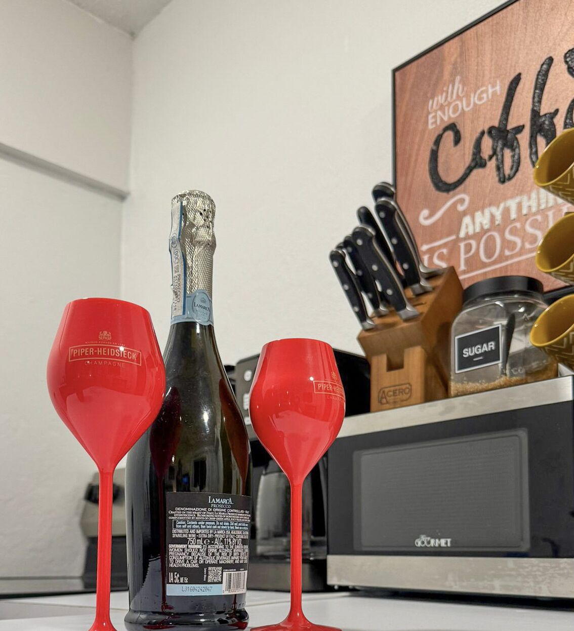 A kitchen counter with a bottle of champagne, two red wine glasses, and a sign that reads "with enough coffee anything is possible."