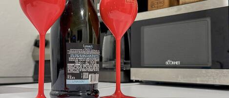 A kitchen counter with a bottle of champagne, two red wine glasses, and a sign that reads "with enough coffee anything is possible."