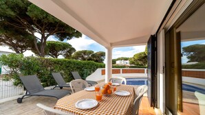 An outdoor dining area with a checkered tablecloth, white chairs, and a view of a swimming pool. - Villa Uno by HelloVacations (Loulé)