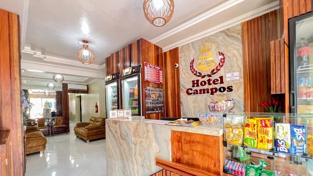 Zona de recepción de un hotel con mostrador de mármol, paneles de madera y un letrero que dice "Hotel Camposos".