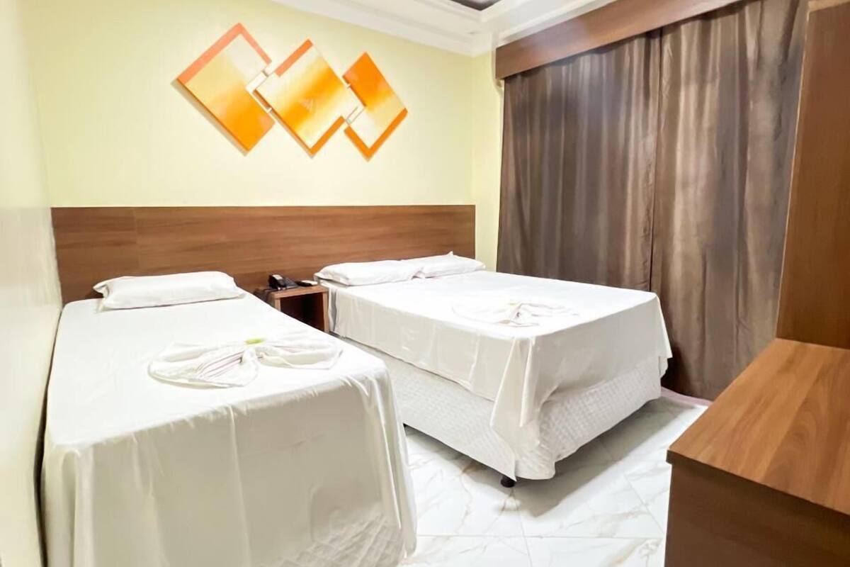 Habitación de hotel con dos camas individuales, cabecero de madera, suelo de mármol y lámpara moderna en el techo.