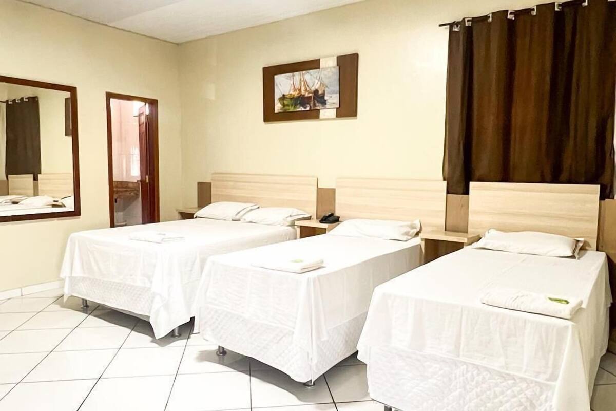Una habitación de hotel con dos camas individuales, un espejo grande, un cuadro en la pared y una cortina en la ventana.