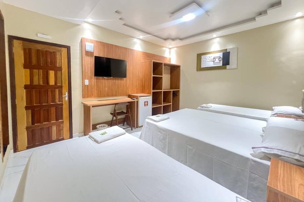 Una habitación con dos camas, un escritorio de madera, televisor y un refrigerador pequeño.