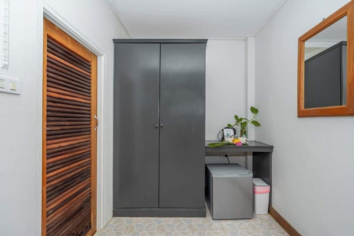 Um corredor estreito com um guarda-roupa cinzento, uma pequena escrivaninha com uma planta e um cesto de lixo.