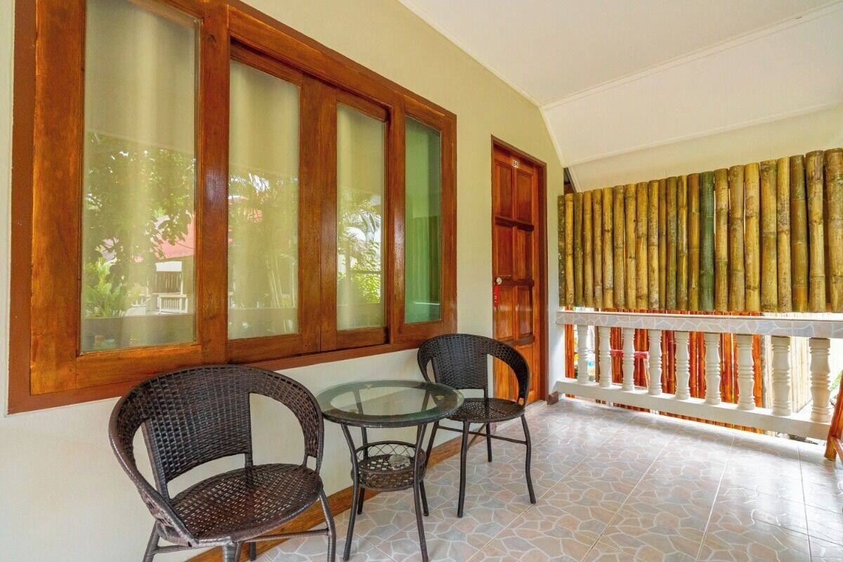 Varanda com cadeiras de vime, mesa de vidro, janelas com moldura de madeira e guarda-corpo de bambu.