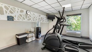 Une salle de sport équipée d’un tapis de course, d’un distributeur d’eau, d’une horloge et d’une fenêtre donnant sur des arbres.