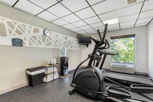 Un gimnasio con cinta de correr, dispensador de agua, reloj y ventana con vista a árboles.
