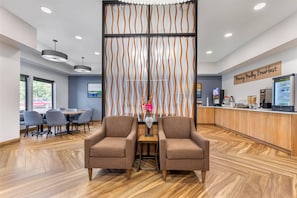 A reception area with a wooden reception desk, two brown armchairs, a decorative wall, and a dining area with gray chairs and a table. - Sleep Inn Manassas, VA (Manassas)