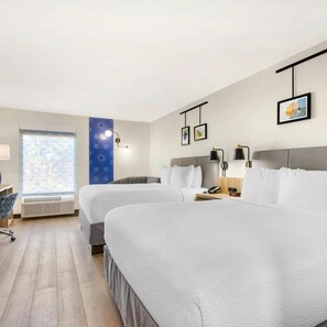 Quarto de hotel com duas camas, uma escrivaninha, uma cadeira, uma janela com vista e um painel com quadros.