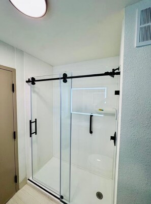 A glass-enclosed shower with a horizontal bar, a door with a handle, and a small shelf with a bottle. - Sleep Inn Manassas, VA (Manassas)