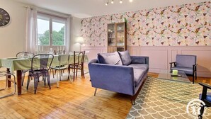 En stue med en blå sofa, spiseområde med dug i tern og en dekorativ væg med blomstermønster.
