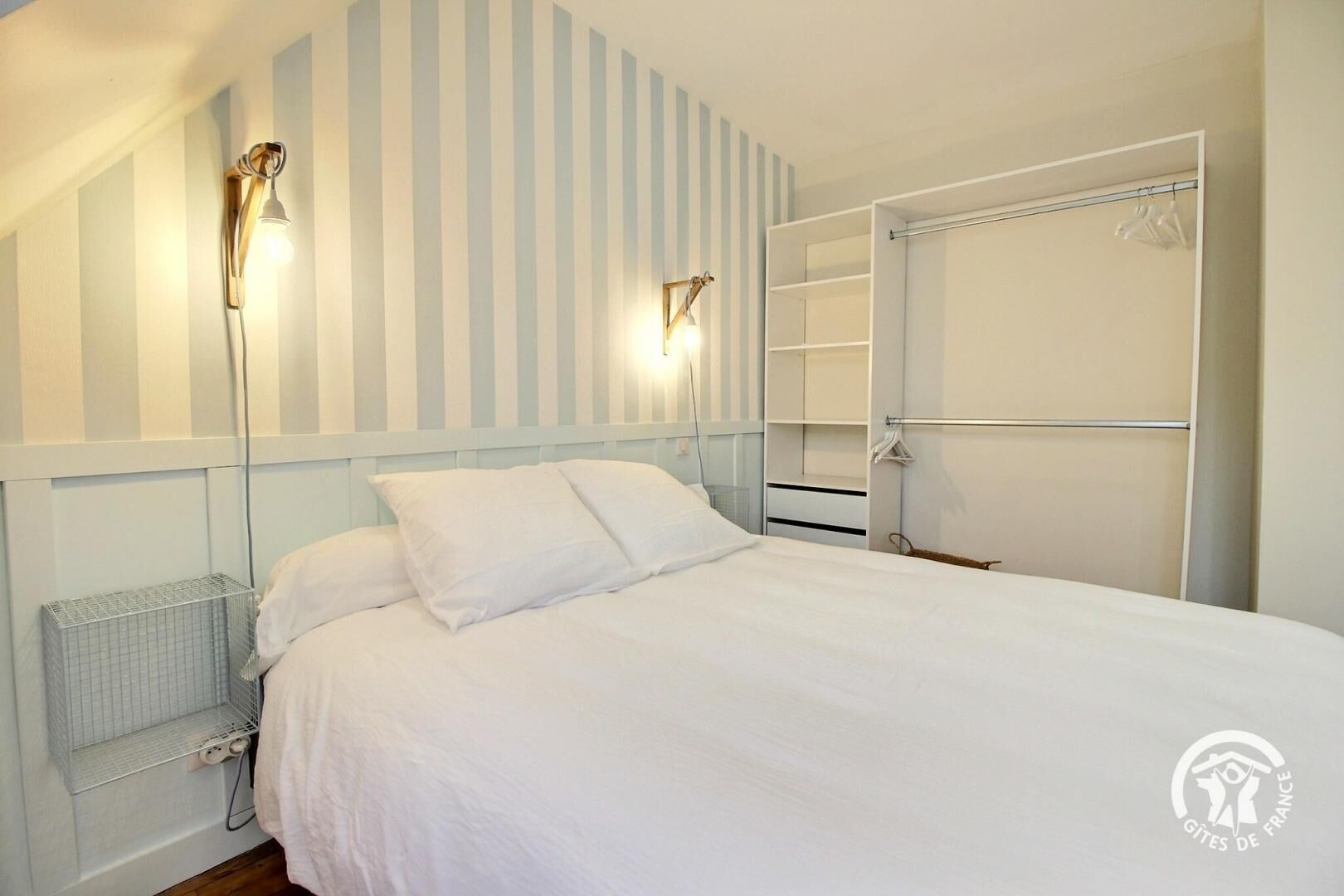 Un dormitorio con cama, radiador, armario y dos luces fijadas a la pared.