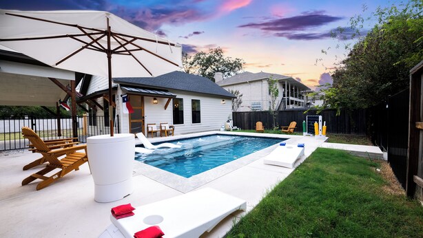A backyard with a swimming pool, lounge chairs, and a patio umbrella.