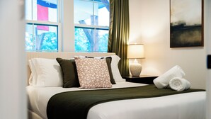 A neatly made bed with white and green bedding, a lamp on the nightstand, and a window with curtains.