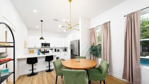 A modern kitchen with white cabinets, a central island, and a dining area with a round table and green chairs.
