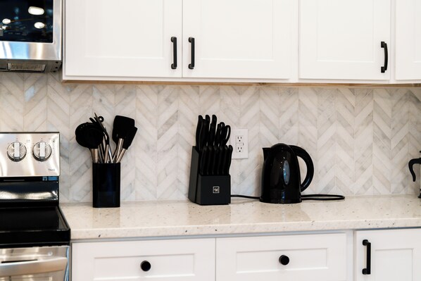 Una cocina con gabinetes blancos, una estufa de acero inoxidable, una cafetera y un bloque de cuchillos sobre la encimera.