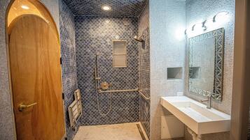 A bathroom with a wooden door, a shower with a blue patterned wall, and a white sink with a large mirror.