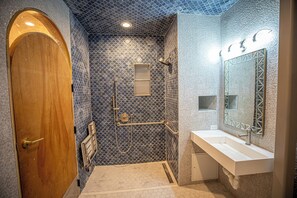 A bathroom with a wooden door, a shower with a blue patterned wall, and a white sink with a large mirror. - Social Stays On State Street (Santa Barbara)