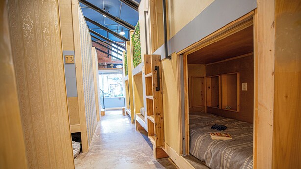 A narrow corridor with wooden bunk beds, each marked with a number. - Social Stays On State Street (Santa Barbara)