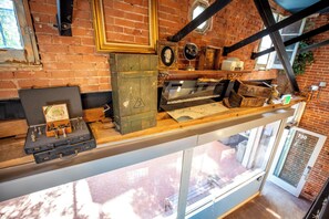 A room with a brick wall, a wooden shelf with various items, a window, and a door with the number 730. - Social Stays On State Street (Santa Barbara)