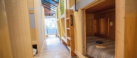 A narrow hallway with wooden walls and a single bed with a striped bedspread.