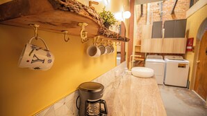 A kitchen with a coffee maker, hanging mugs, and a brick wall. - Social Stays On State Street (Santa Barbara)
