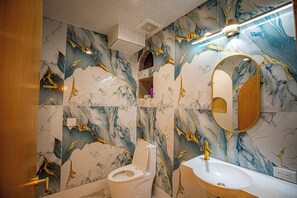 A bathroom with marble walls, a toilet, a sink, and a mirror. - Social Stays On State Street (Santa Barbara)