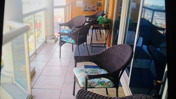 A balcony with wicker chairs and a table, overlooking a cityscape.