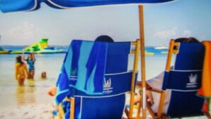 Escena de playa con una sombrilla azul, una silla de playa y una torre de salvavidas.