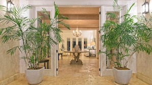 A spacious hallway with a marble floor, flanked by large potted plants, leading to a dining area with a chandelier. - Tortuga A2 - Charming Villa in Exclusive Beach and Golf Resort (Punta Cana)