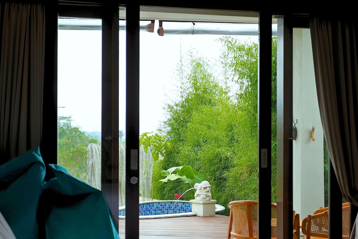 A room with a sliding glass door leading to an outdoor area with a pool, chairs, and a statue.