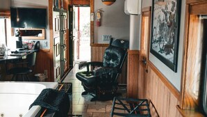 A room with a wooden ceiling, a black leather chair, a bathtub, and a dining area with a TV. - Easy Rider Railroad Caboose Cabin (Upper Lake)