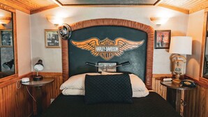 A room with a Harley-Davidson logo on the headboard, a bed with white and black bedding, a lamp on a bedside table, and a mirror on the wall. - Easy Rider Railroad Caboose Cabin (Upper Lake)