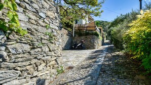 A narrow cobblestone street flanked by stone walls and lush greenery, with a parked motorcycle and a wooden structure in the background. - 2 bedroom gorgeous apartment in Semorile (Semorile)