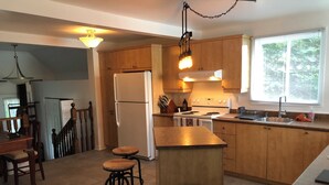 Une cuisine moderne avec des meubles en bois, un réfrigérateur en acier inoxydable, une cuisinière à gaz et une fenêtre équipée de stores.