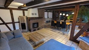 Een gezellige woonkamer met een open haard, een eethoek met een tafel en stoelen, en een keuken met een bakoven.