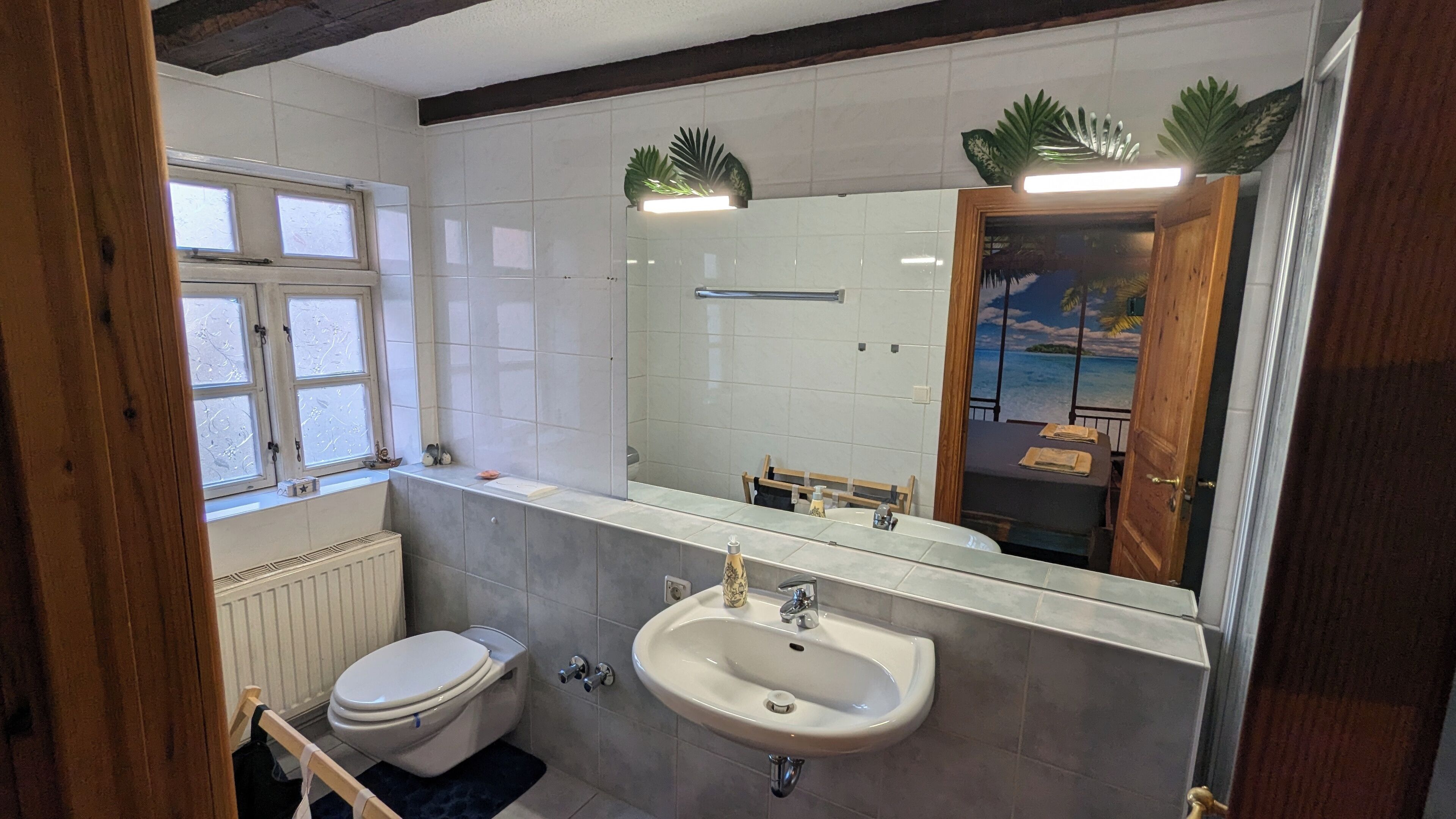 A bathroom with a toilet, sink, and a large mirror.