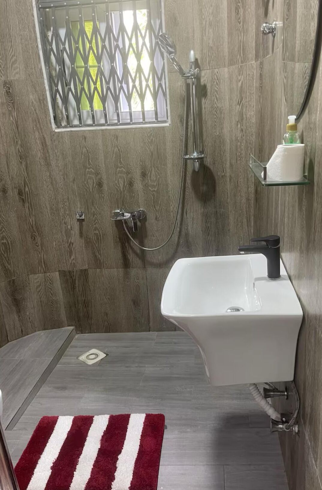 Une salle de bain avec une douche, un lavabo et une fenêtre ornée d’un motif en treillis.