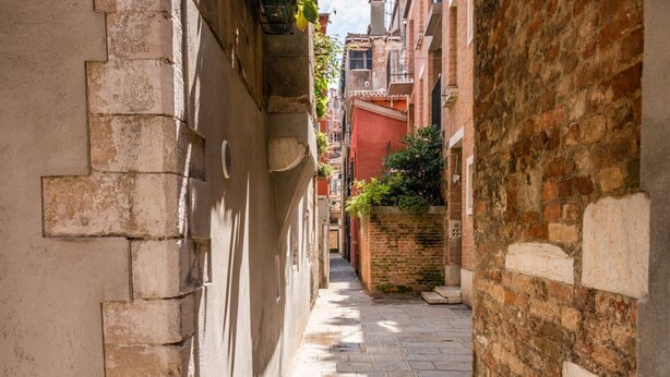 A narrow stone-paved alleyway between buildings with a brick wall on the right and a stone wall on the left. - Ramo delle Moschette (Venezia)