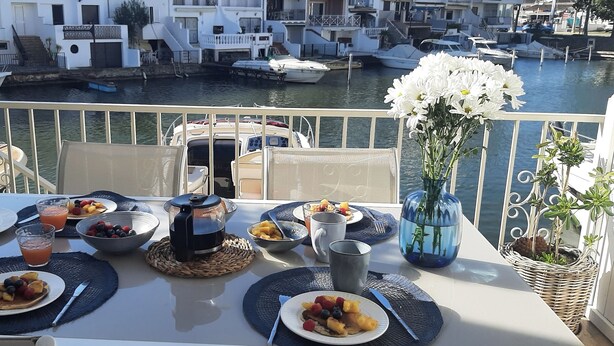 A balcony table set with breakfast items, a coffee maker, and a vase of flowers. - Fishermen's house with 4 x 8 m mooring line available (Empuriabrava)