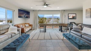 A spacious living room with a large window, a ceiling fan, and a dining area with a table and chairs. - Havasu Cotati - Pool, Spa, FirePit, Games, Garage (Lake Havasu City)