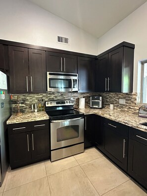 A kitchen with dark cabinets, stainless steel appliances, and a tiled backsplash.