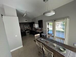 A modern kitchen with dark cabinetry, a central island, and a dining area with a table and chairs.