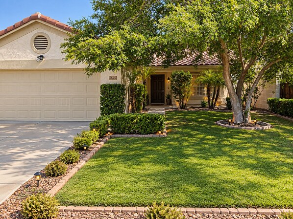 A residential house with a garage, a well-maintained lawn, and a tree in the front yard.